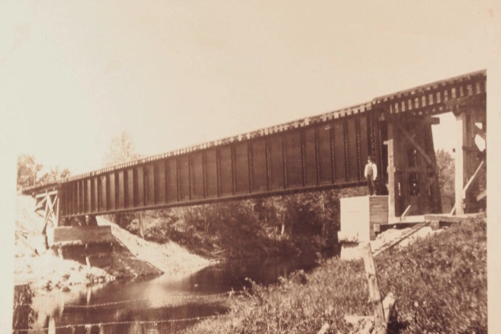 A brown and beige photo of a 1922 bridge across a river near Embrun